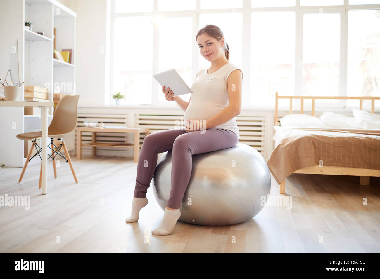 Happy pregnant woman bouncing on exercise ball with young daughter in a