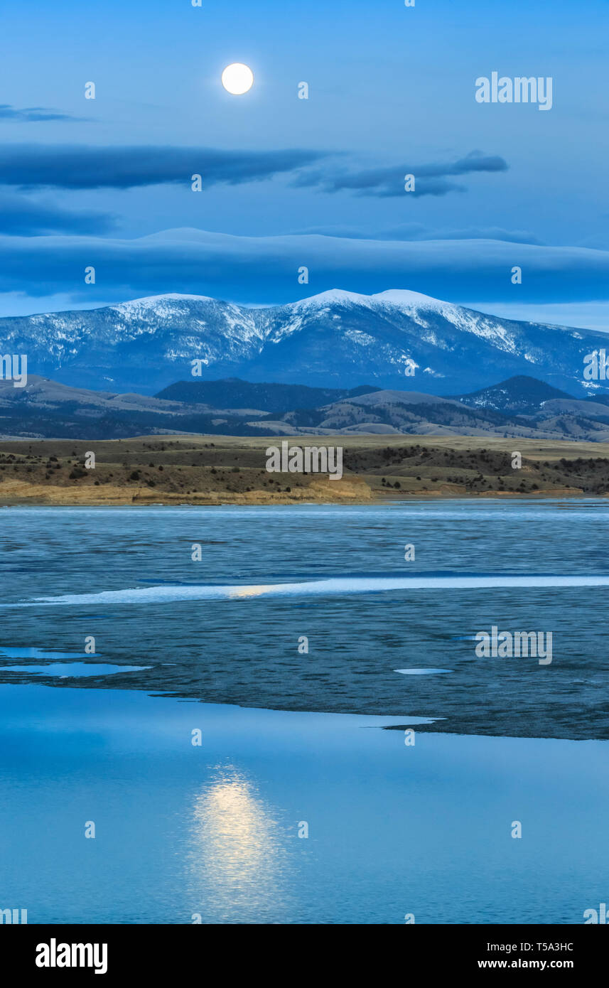 full moon rising behind mount baldy above ice breakup on canyon ferry lake near townsend, montana Stock Photo