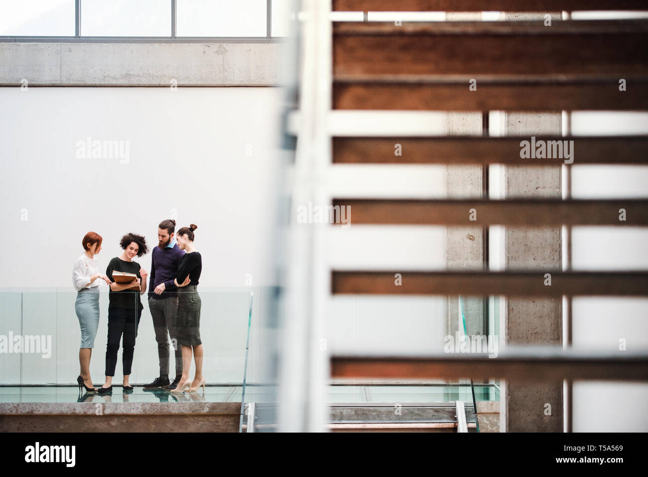 A group of young businesspeople standing near staircase, talking. Stock Photo