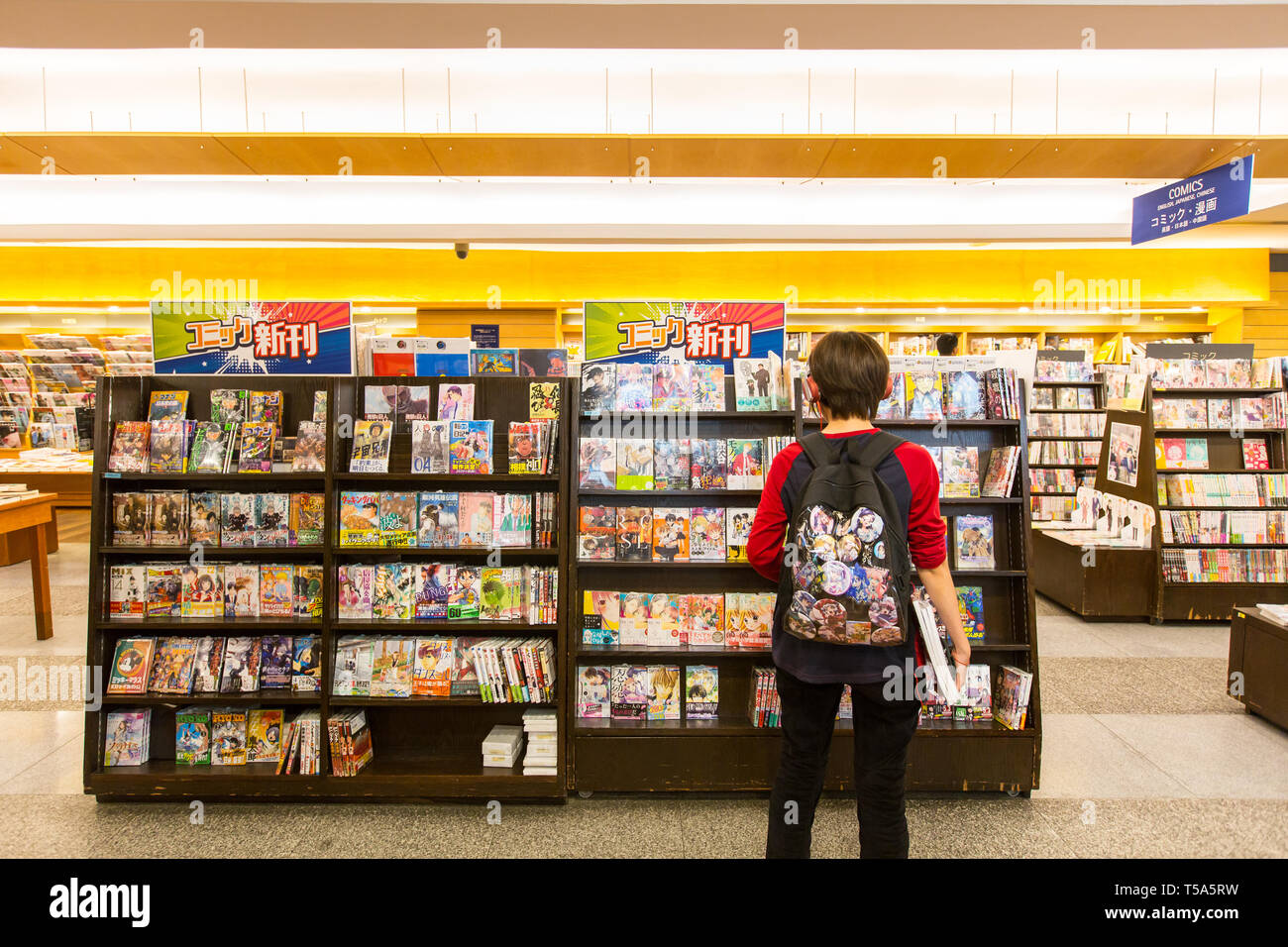 A hippie customer wearing backpack is checking out the newest release of popular manga on the shelves in Kinokuniya, Singapore. Stock Photo
