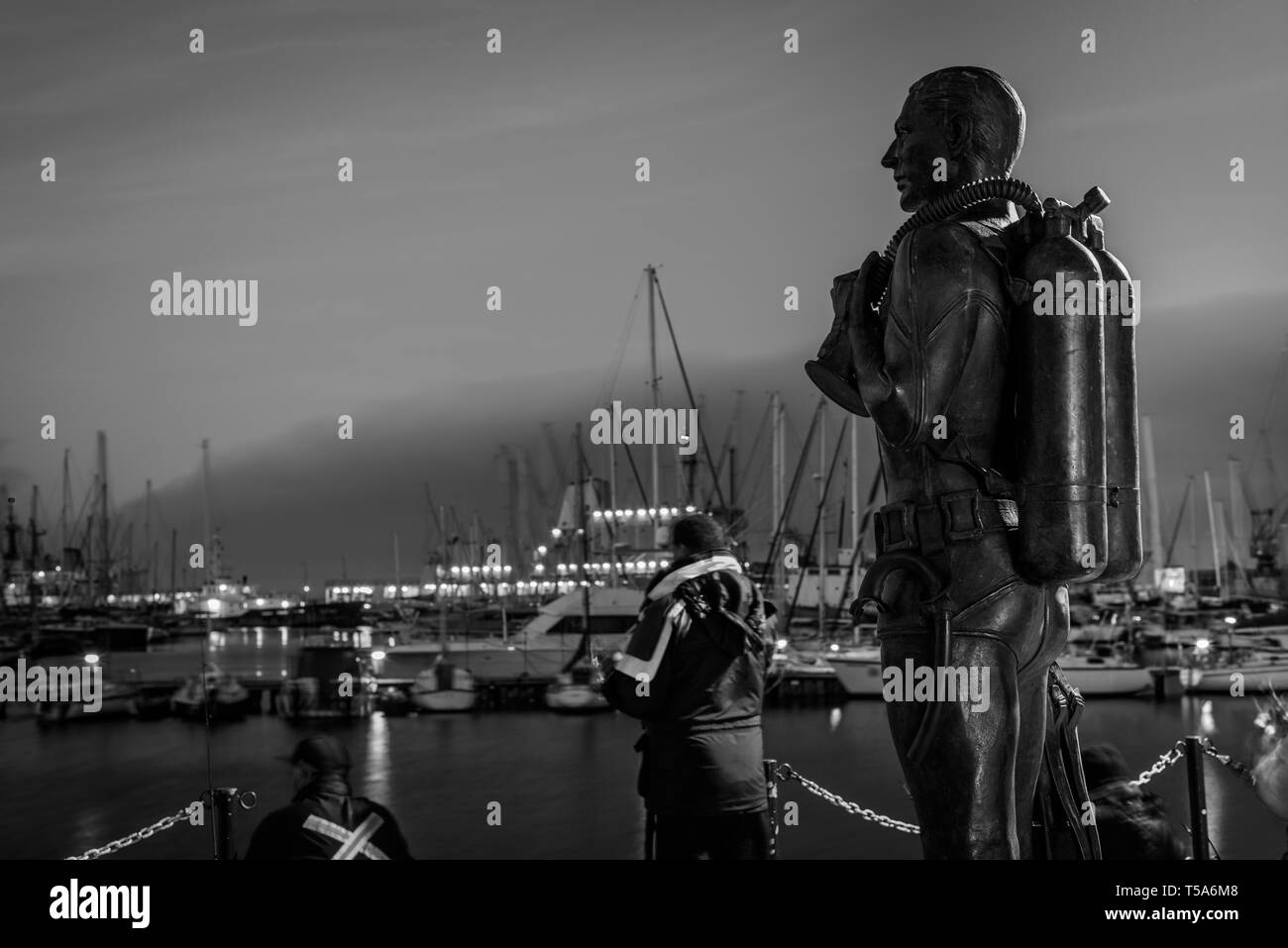 Fishermen at the Simons Town marina in South Africa's Western Cape province in the shadow of the Standby Diver bronze sculpture memorial Stock Photo
