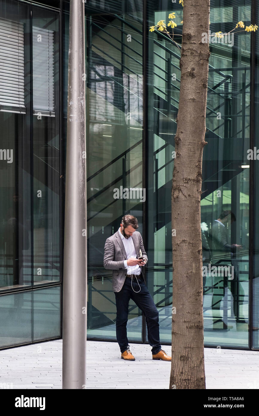 A man standing in front of a glass fronted building using his smartphone. Stock Photo