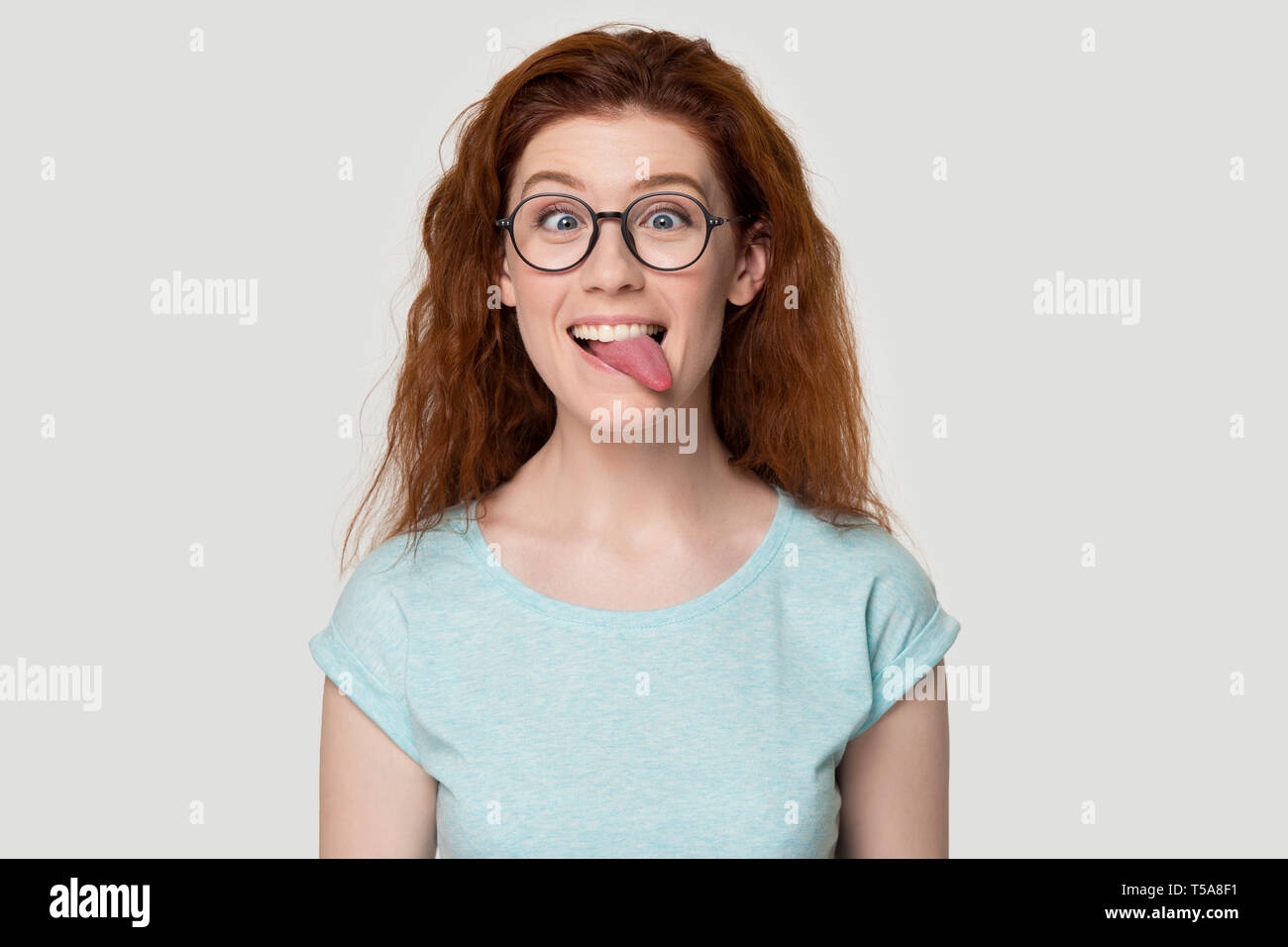 Funny red-haired girl in glasses play childish showing tongue Stock Photo