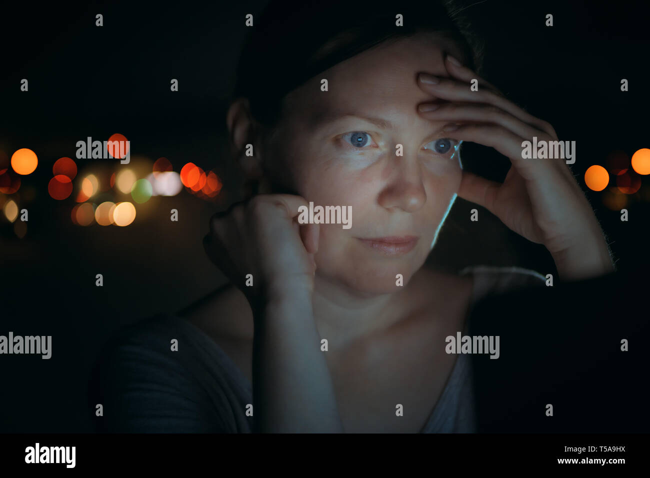Low key portrait of tired woman looking at laptop computer screen exposed to the effect of technology blue light that impacts on sleep and circadian r Stock Photo