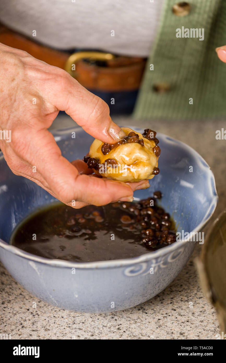 Woman dipping golf ball-sized pieces of Monkey Bread dough into a mixture of melted butter, brown sugar and currants.  (MR) Stock Photo