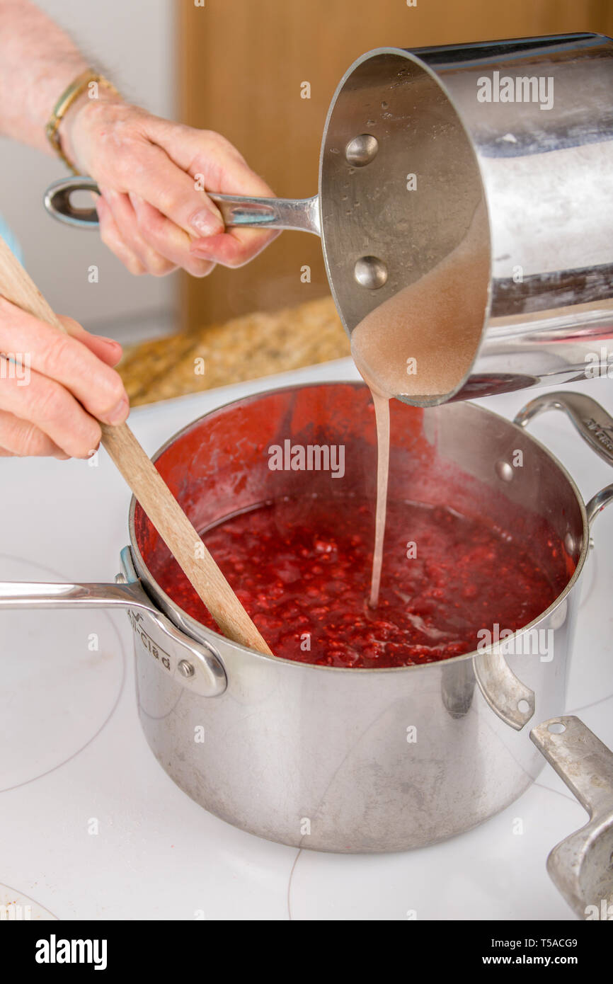 Woman pouring fruit pectin and water mixture into raspberries as a part of making raspberry jam.  (MR) (PR) Stock Photo
