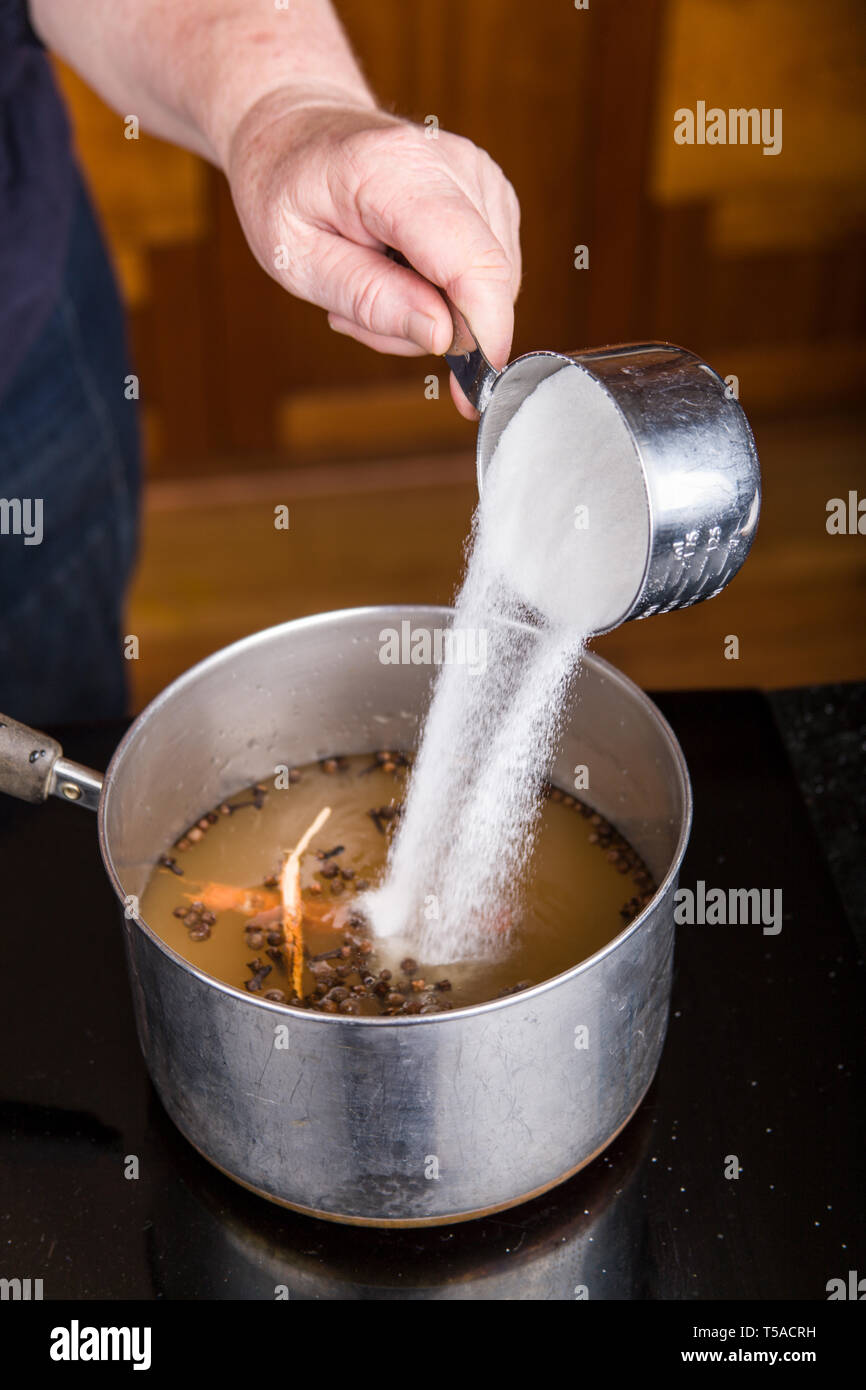 Woman pouring sugar into the pickling solution of apple cider vinegar, raw cinnamon, whole allspice and whole cloves to be used in canning pickled bee Stock Photo