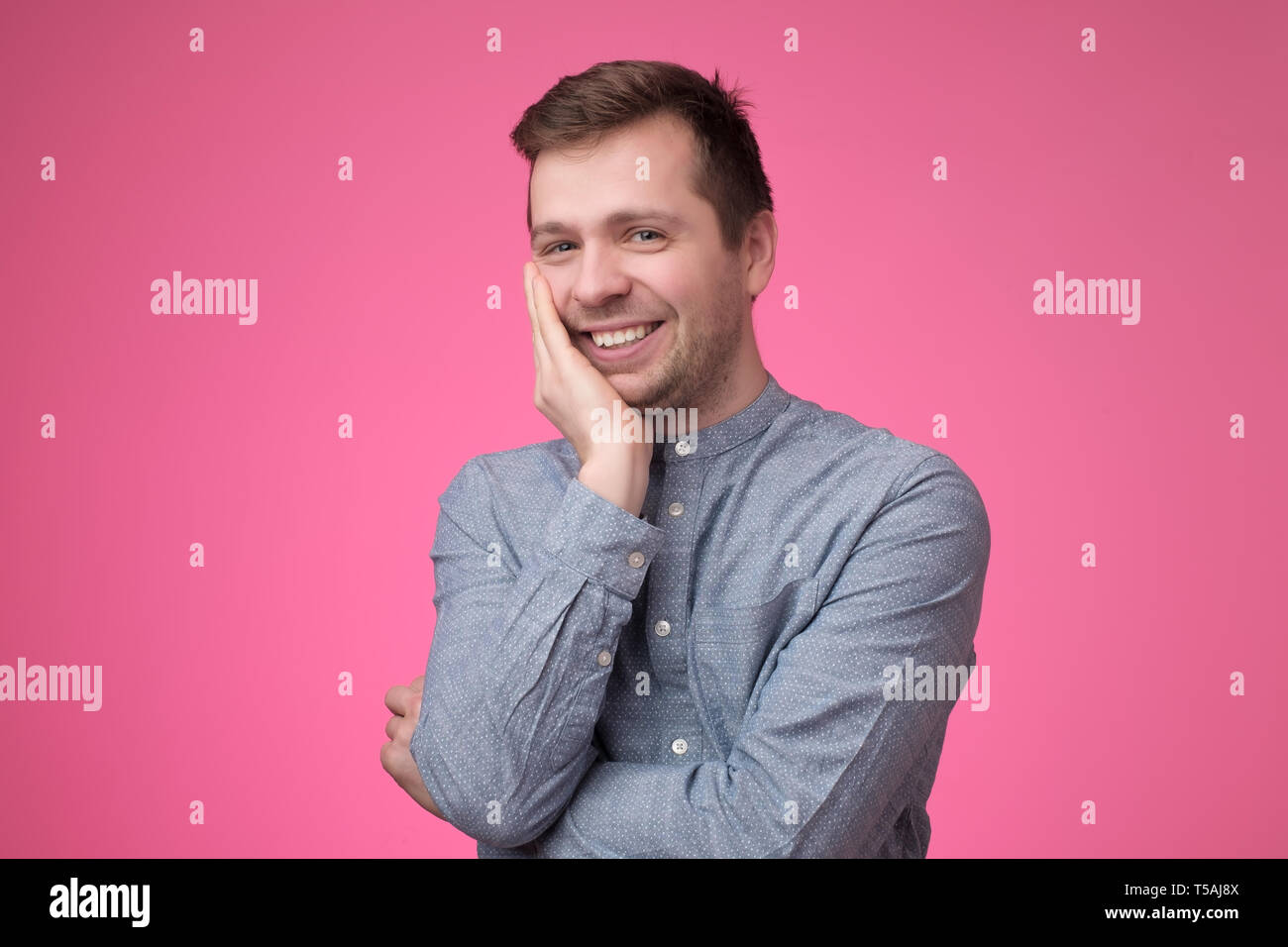 Smiling young caucasian man putting his hand to his chin Stock Photo