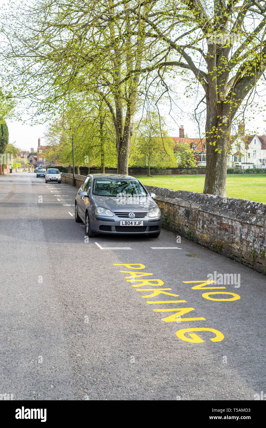 No parking sign in yellow paint on road surface with car parked in designated resident parking bay Stock Photo