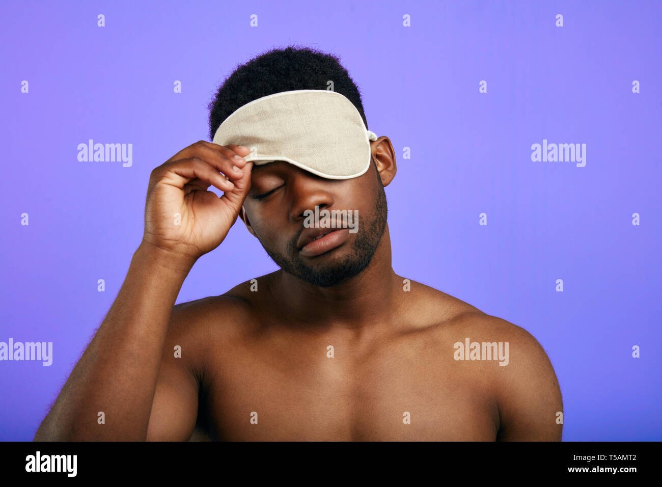 sleepy tired man taking off or putting on the sleeping mask. close up portrait. isolated blue background.tiredness concept. Stock Photo