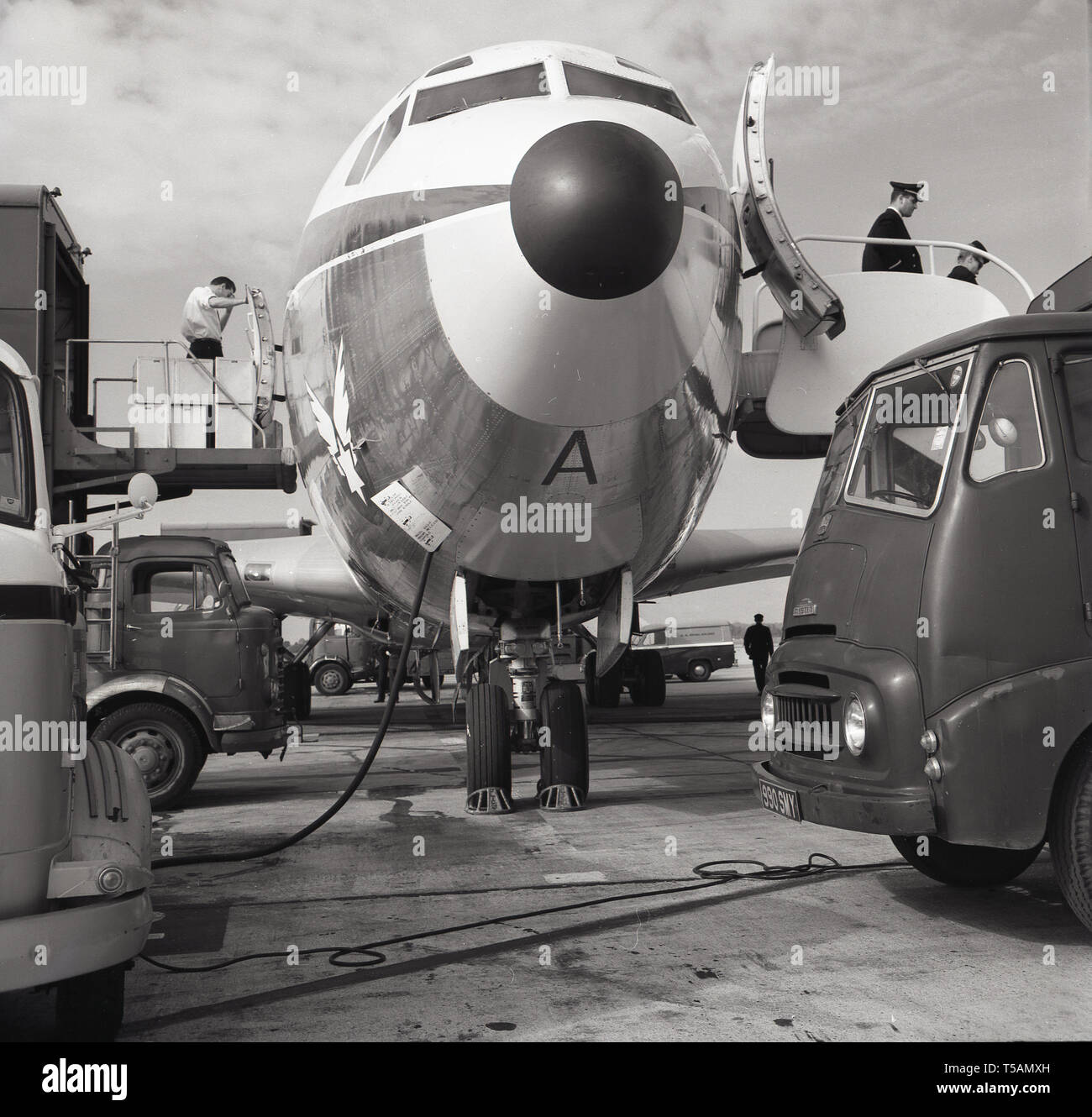 1960, historical, front view of a jet aircraft nose cone and cockpit as service trucks and freight loaders surround the plane parked at London (Heathrow) Airport, England. Stock Photo