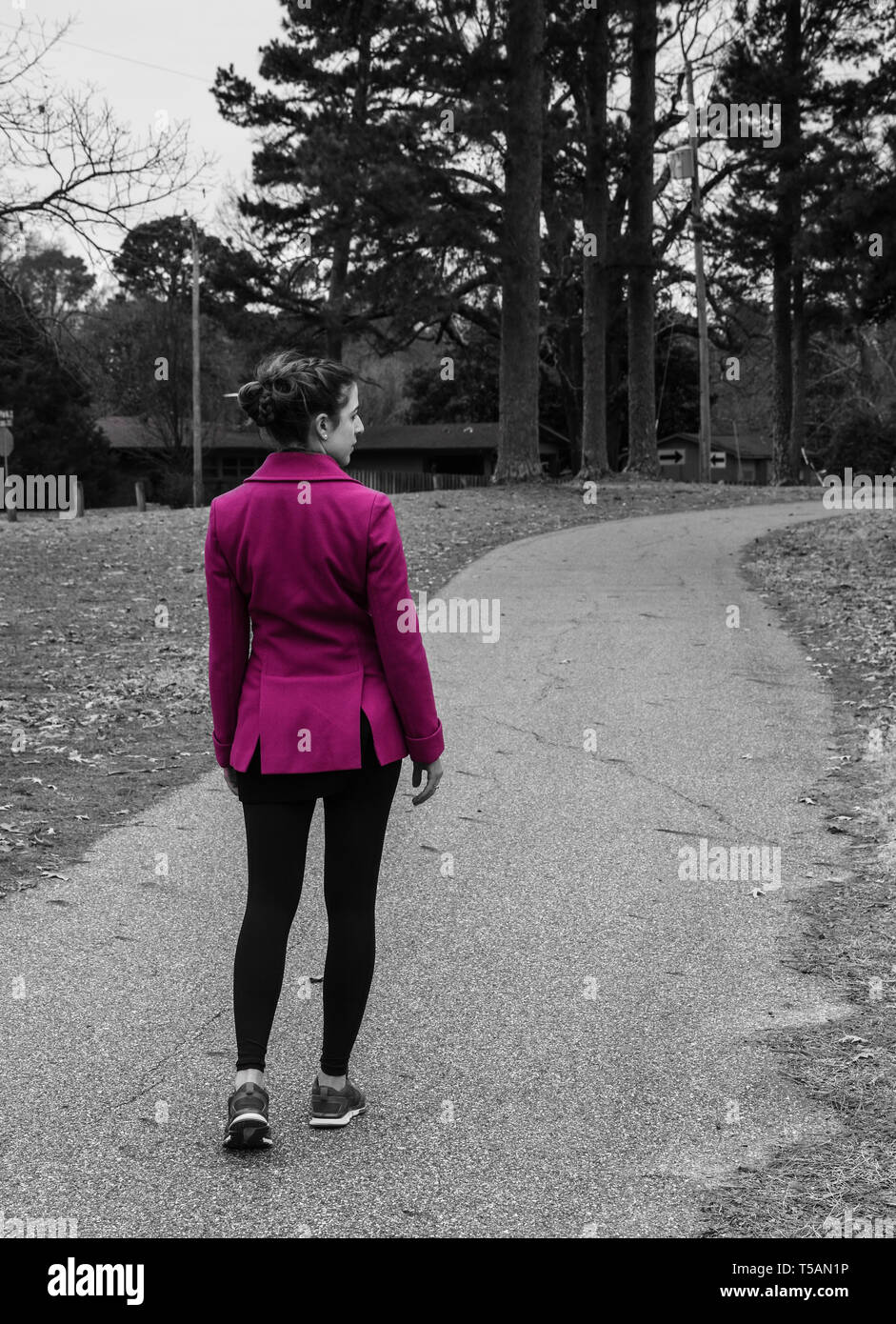 Black white back, profile view of young woman with braided hair walking on curving path, bright pink jacket, coat, color spot,  color Stock Photo