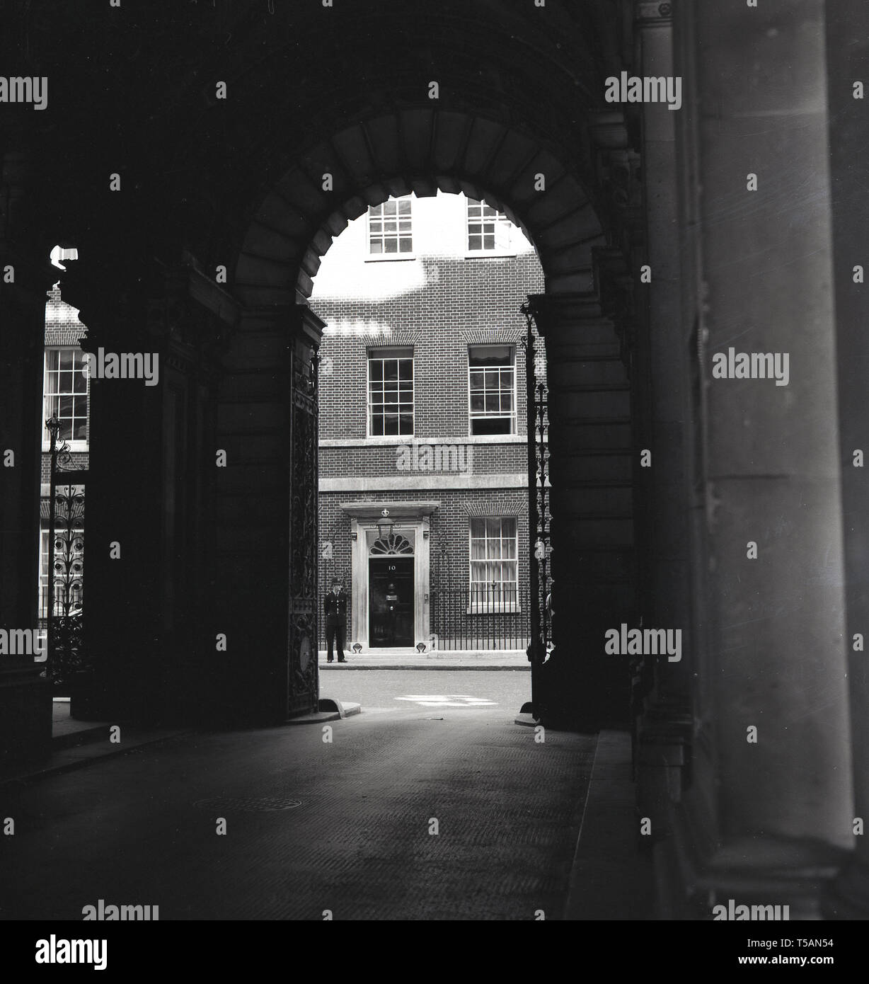 1960s, historical, a view through an archway of No 10 Downing Street, London, home of the Prime Minister of the UK, with a British policeman standing in attendance. Orginally three georgian houses, they were given to the First Lord of the Treasury by King George II and made into one house by William Kent for Sir Robert Walpole. Stock Photo