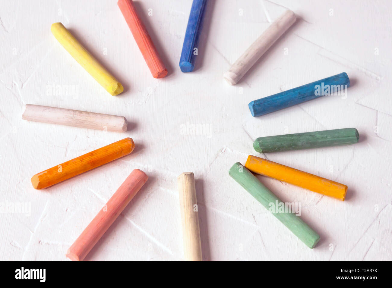 row of mixed color of used chalk pastel sticks crayon sun rays circle isolated on white