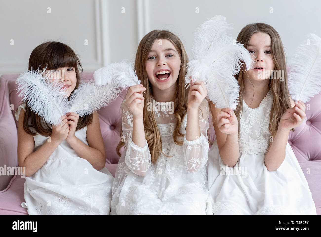 Three funny girls play, they are hiding behind feathers Stock Photo - Alamy