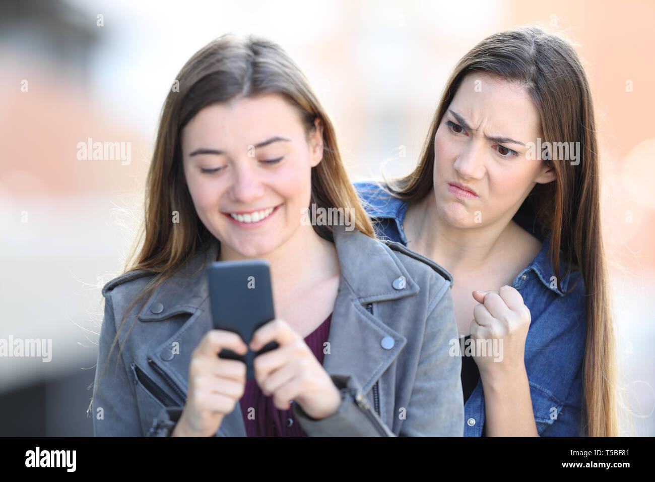 Angry girl spying the smart phone of a friend in the street Stock Photo