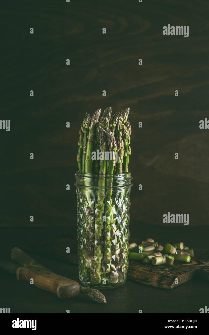 Green asparagus in glass jar with water on table at dark background. Fresh asparagus storage. Spring seasonal vegetables Stock Photo