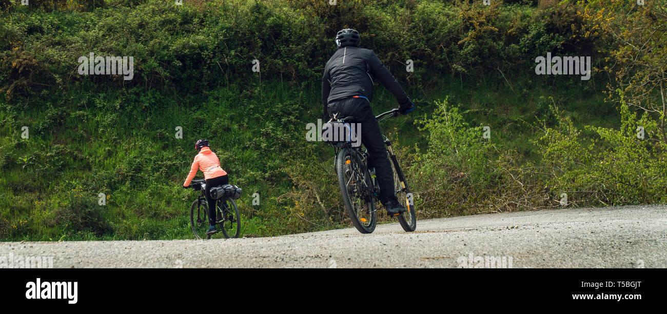 Couple of cyclists riding bicycles in Camino de Santiago, Galicia, Spain. Wide view. Sport banner Stock Photo