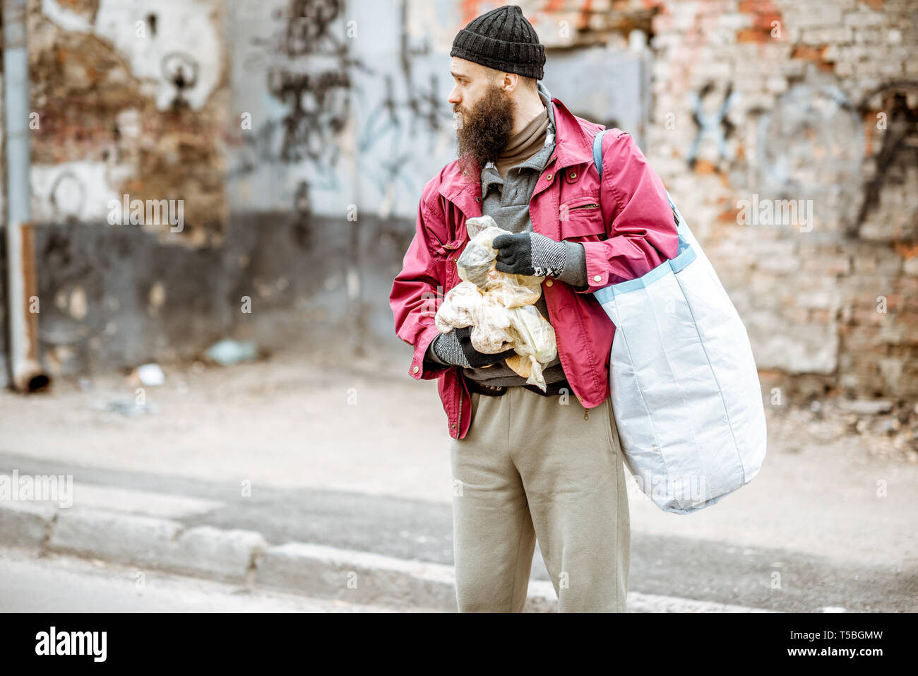Homeless depressed beggar standing with bags on the street on the ragged  wall background. Concept of social poverty Stock Photo - Alamy