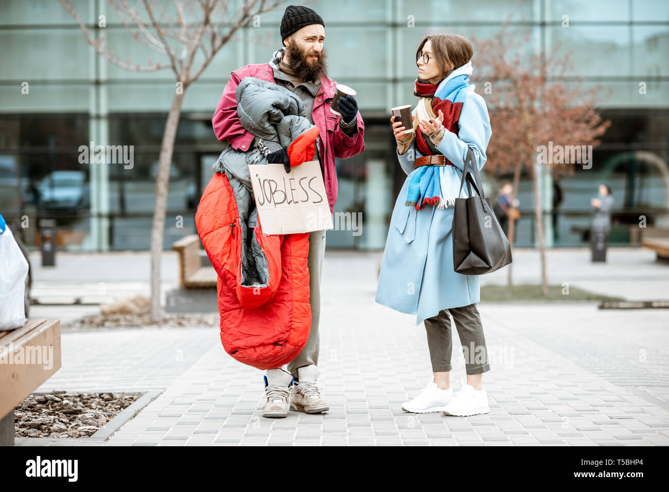 Homeless beggar talking with passing by woman while standing together near the business center. Concept of a human understanding Stock Photo