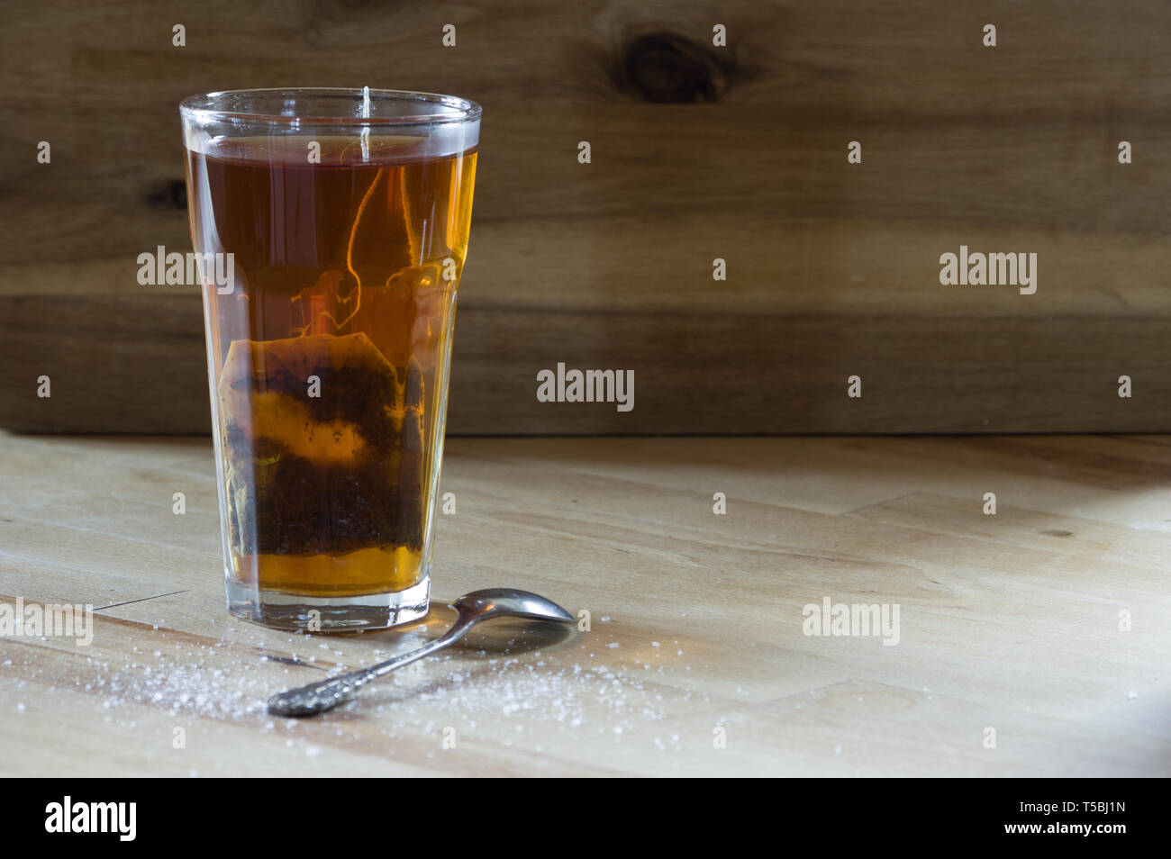 glass of herbal tea on wooden table with sugar sprinkled next to it Stock Photo