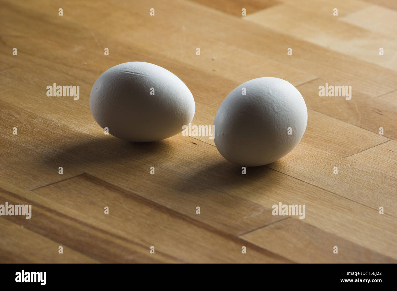 two white eggs laying on a wooden kitchen worktop Stock Photo