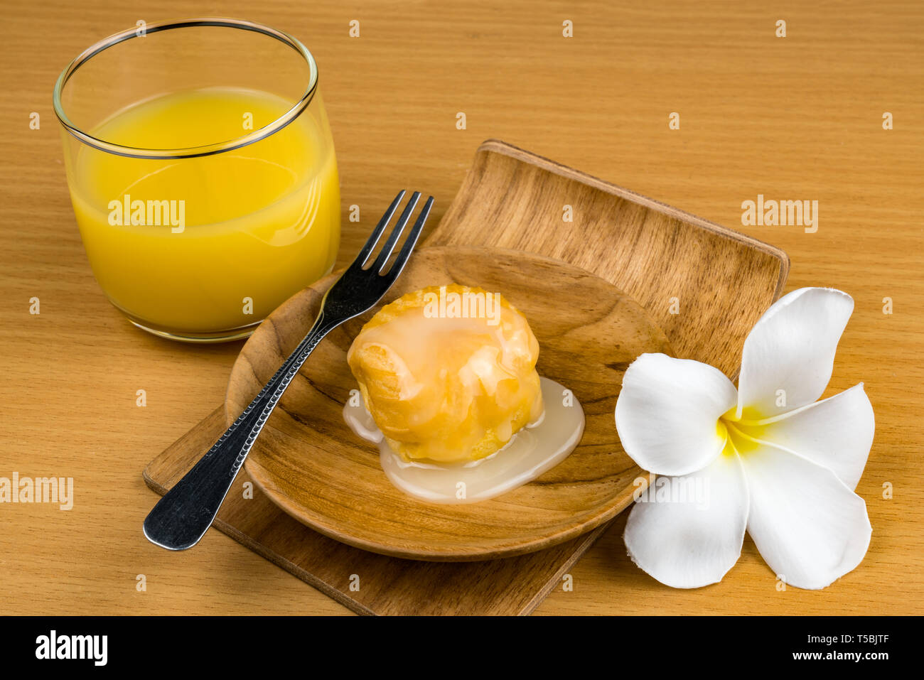 Aclair topped with sweet condensed milk in wooden plate with a glass of passion fruit juice on wooden table Stock Photo