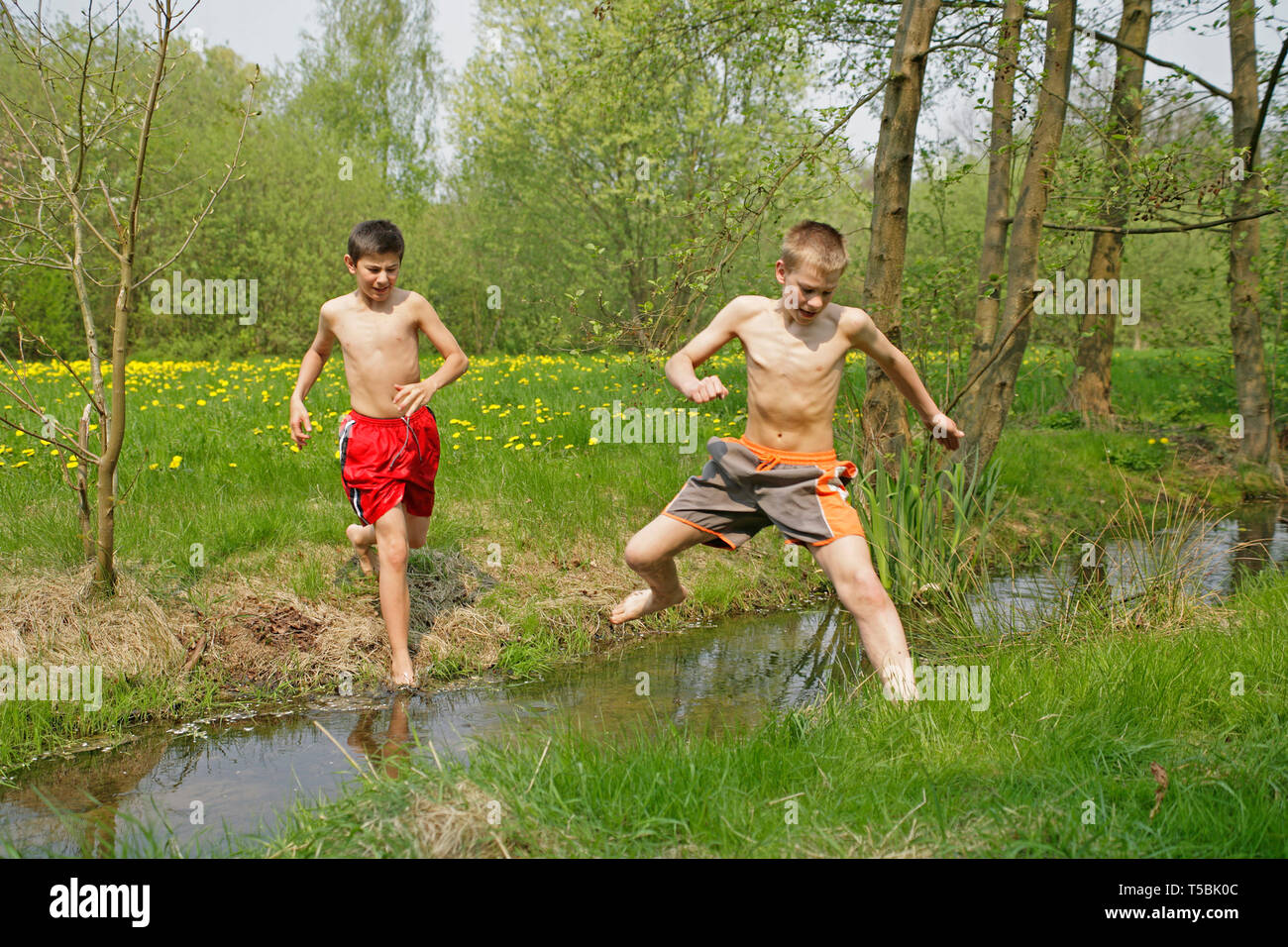 two teenage boys jumping barefoot across a stream Stock Photo Alamy