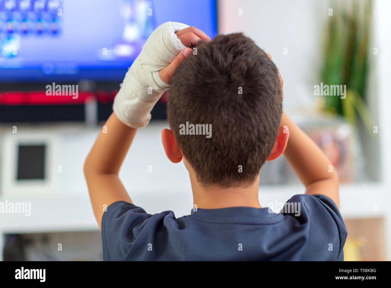 Anonymous boy with broken arm watching TV Stock Photo