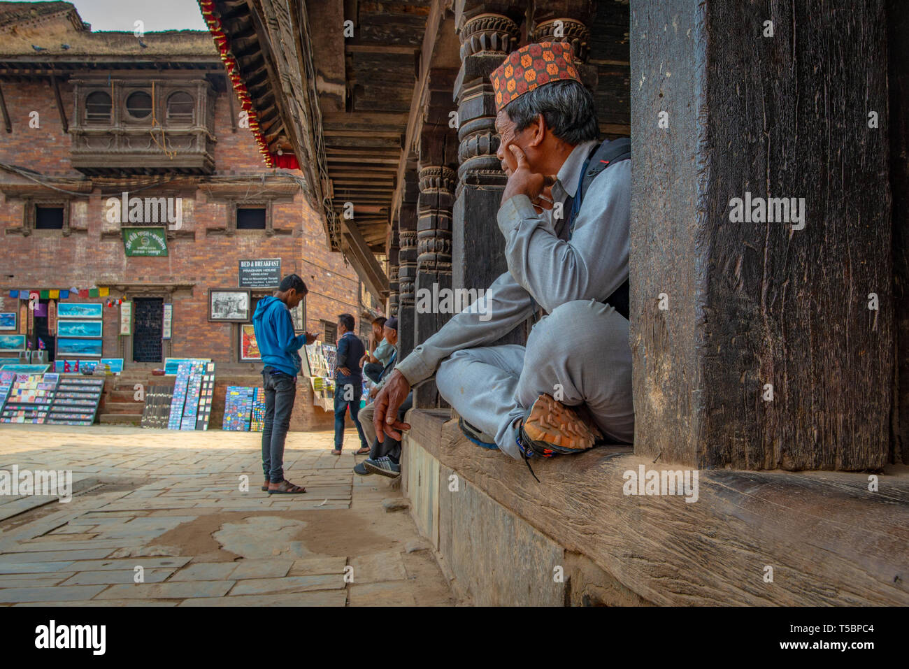 BHAKTAPUR, NEPAL - APRIL 5, 2019: Old man with traditional nepalese hat staring at passers-by Stock Photo