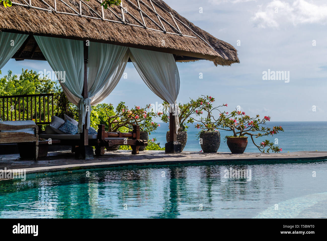 Indonesian bale with beds and flower pots at infinity pool on the cliff with a view of the ocean. Lifestyle, relaxation, tropical holidays. Stock Photo