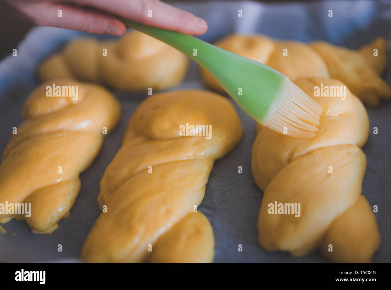 close-up of hand glazing braided sweet yeast bunns using silicone pastry brush before baking Stock Photo