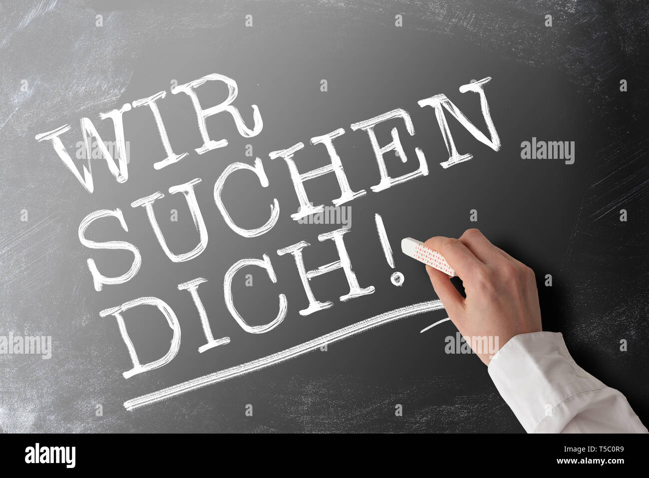 hand holding piece of chalk writing words WIR SUCHEN DICH, German for we are looking for you or we want you, job offer and opportunity concept Stock Photo