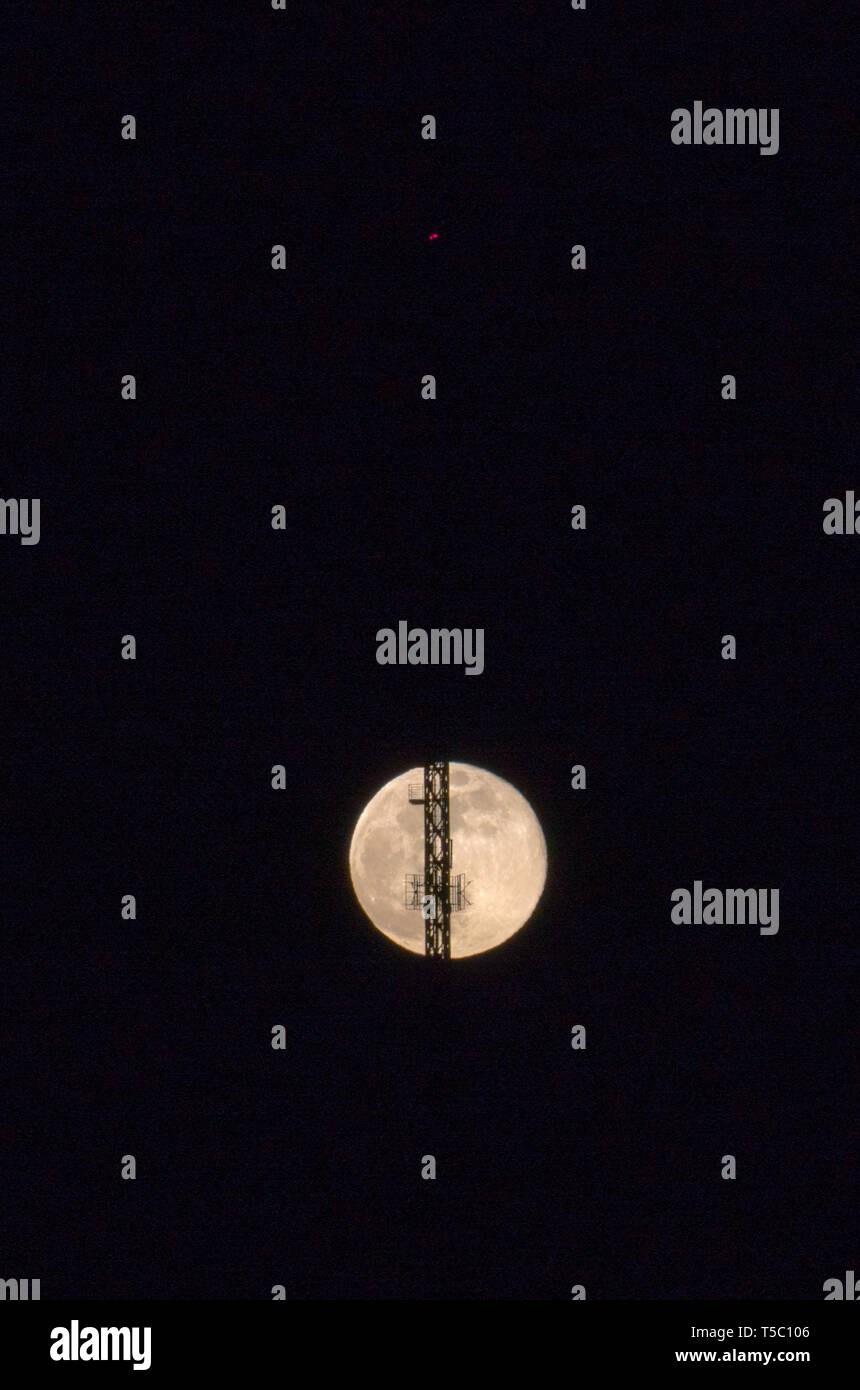 A full moon rising into the night sky with a radio antenna and