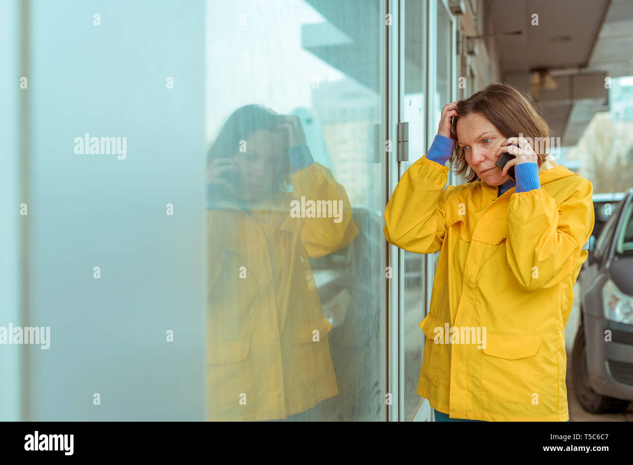 Sad woman in yellow raincoat talking on mobile phone out on the street while it's raining Stock Photo