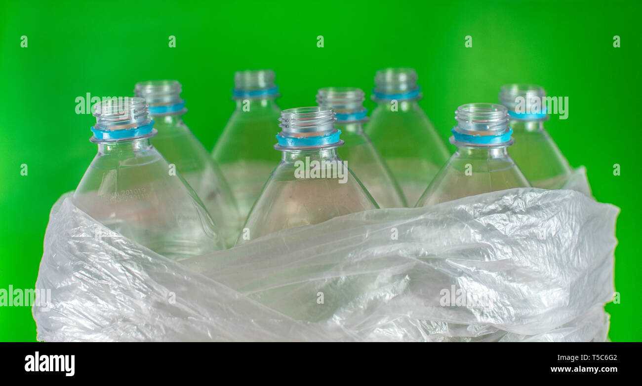 Bottlenecks of a pack of 8 empty and recyclable plastic water bottles, with no caps, blue seal, inside a plastic bag, on a colored vivid green Stock Photo