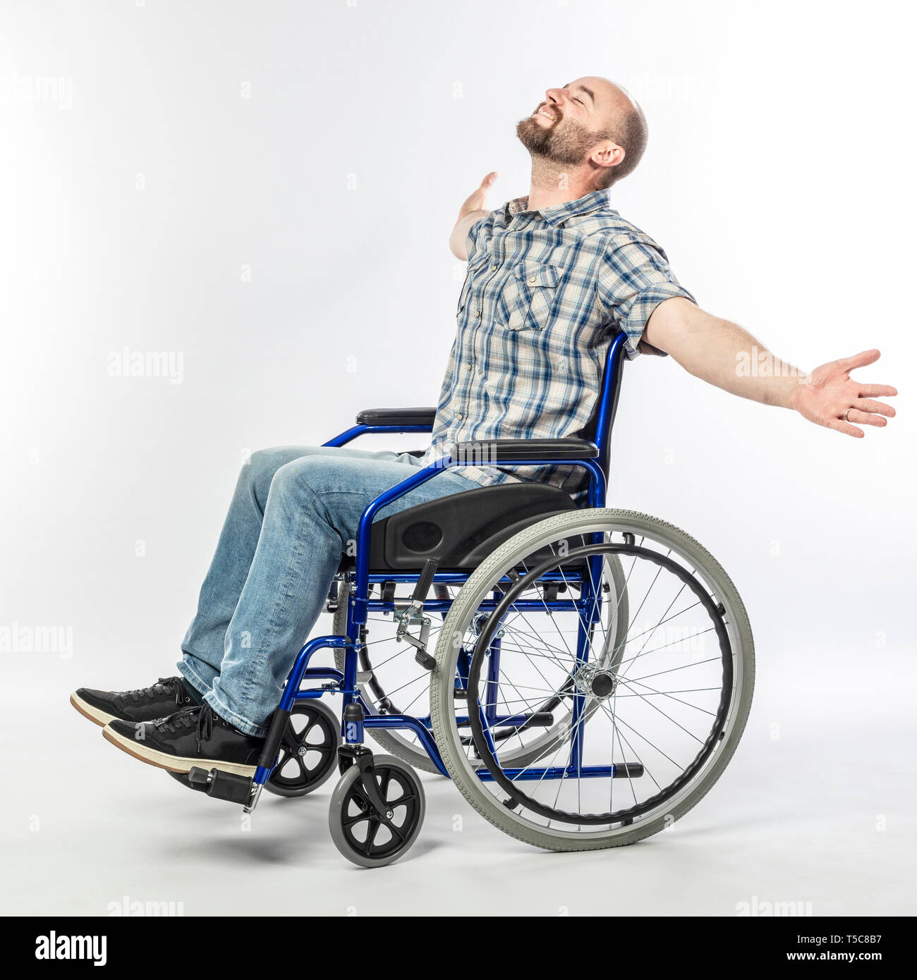 Man sitting in a wheelchair with arms raised and eyes closed. smiling and positive expression. Stock Photo