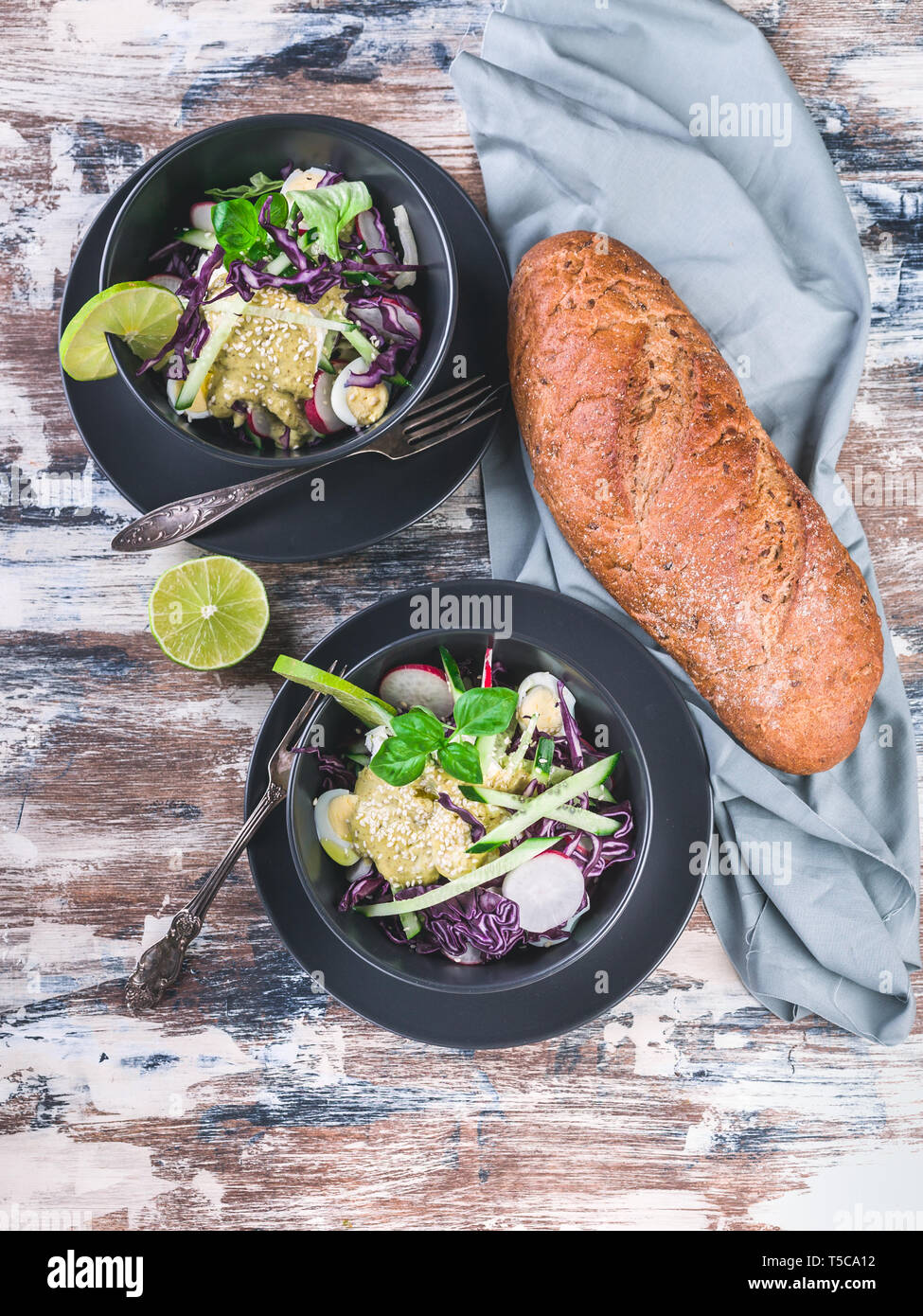 Top view italian ciabatta and fresh vegetable salad in a dark bowl. Salad with radish, red cabbage, cucumber, pesto and sesame seeds. Stock Photo