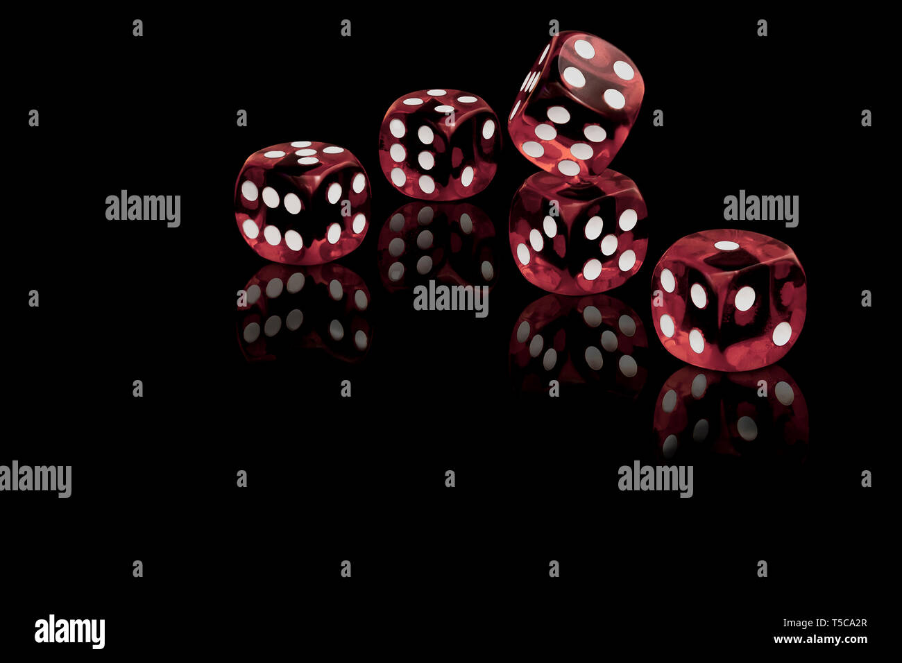 Five red dices isolated on a black background casting a reflection on the surface. Stock Photo