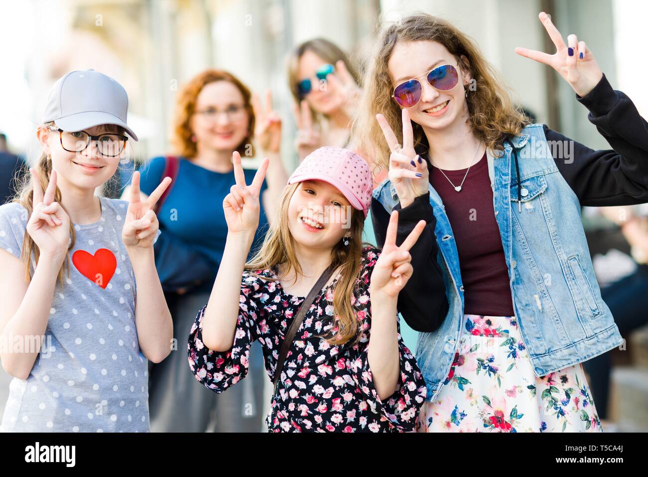Three young girls posing on city streets - showing victory sign with fingers - fun in the city Stock Photo