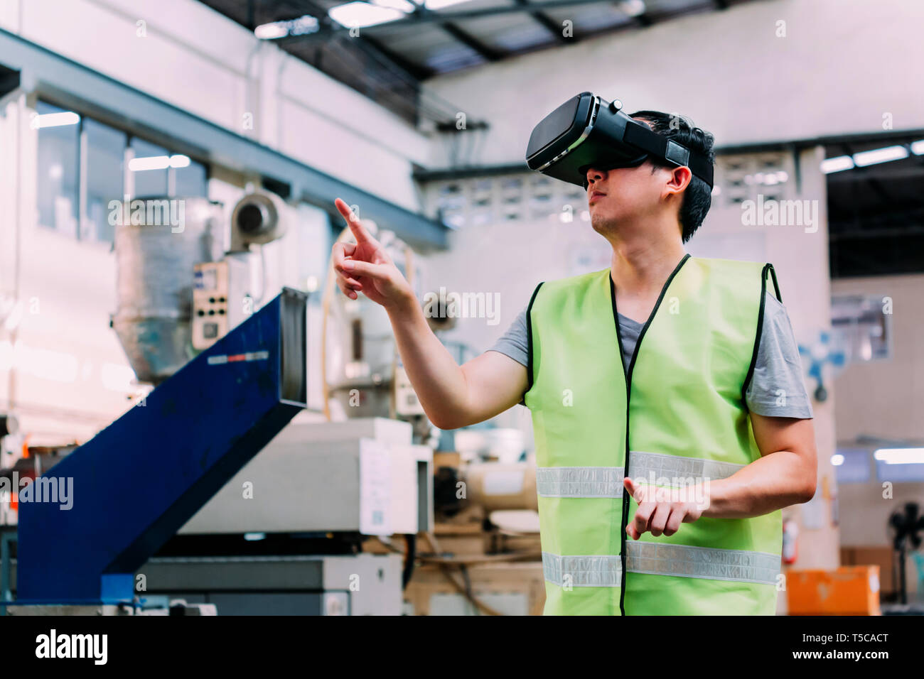 Industrial factory and manfacturing engieering worker wearing VR goggle headset touching in virtual reality simulation alongside heavy duty machines Stock Photo
