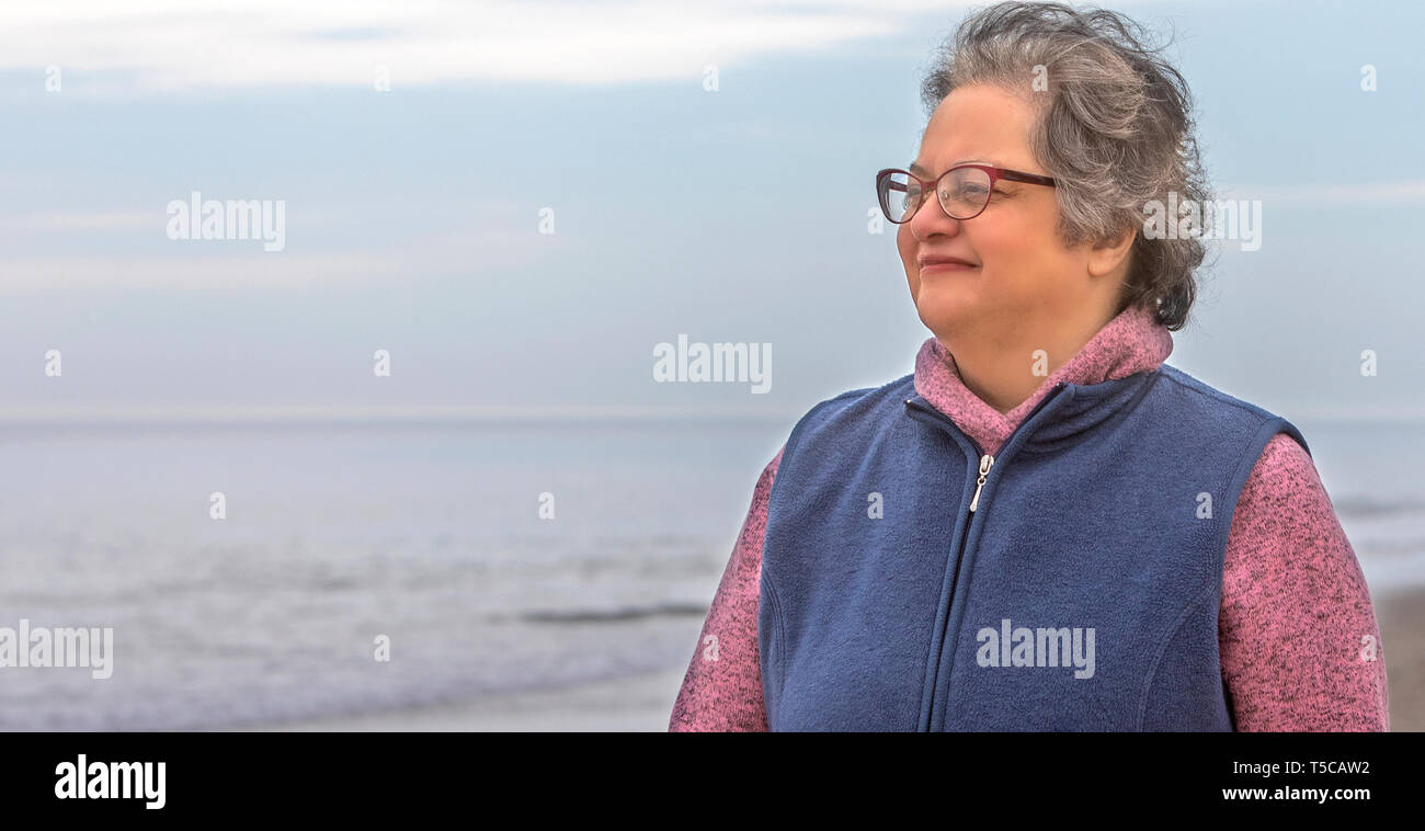 A senior woman enjoying walking in the sand on the beach by the ocean shore. Stock Photo