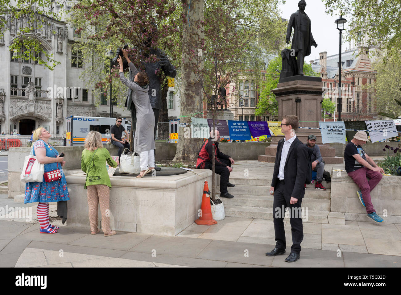 Women campaigners position a large potted tree at the feet of Nelson Mandela's statue in Parliament Square during the week-long protest by climate change activists with Extinction Rebellion's campaign to block road junctions and bridges around the capital, on 23rd April 2019, in London England. Stock Photo