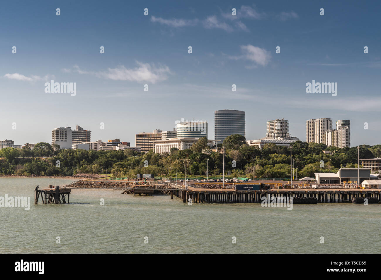 Darwin Australia - February 22, 2019: South side downtown skyline seen from harbour waters. Dock up front. Blue sky and greenish water. Stock Photo