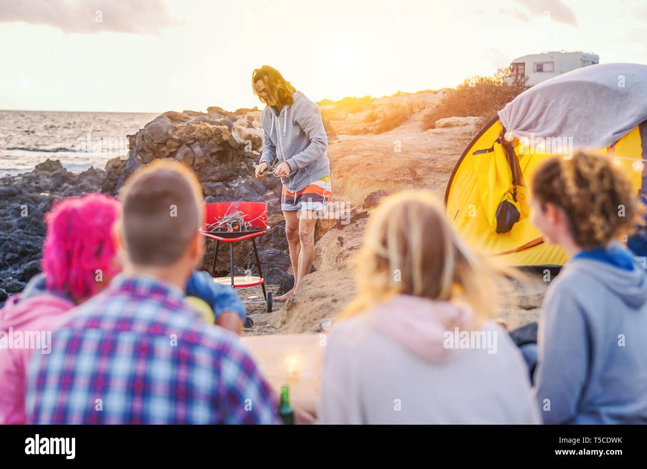Group of happy friends camping with tent on the beach and preparing a barbecue dinner Young