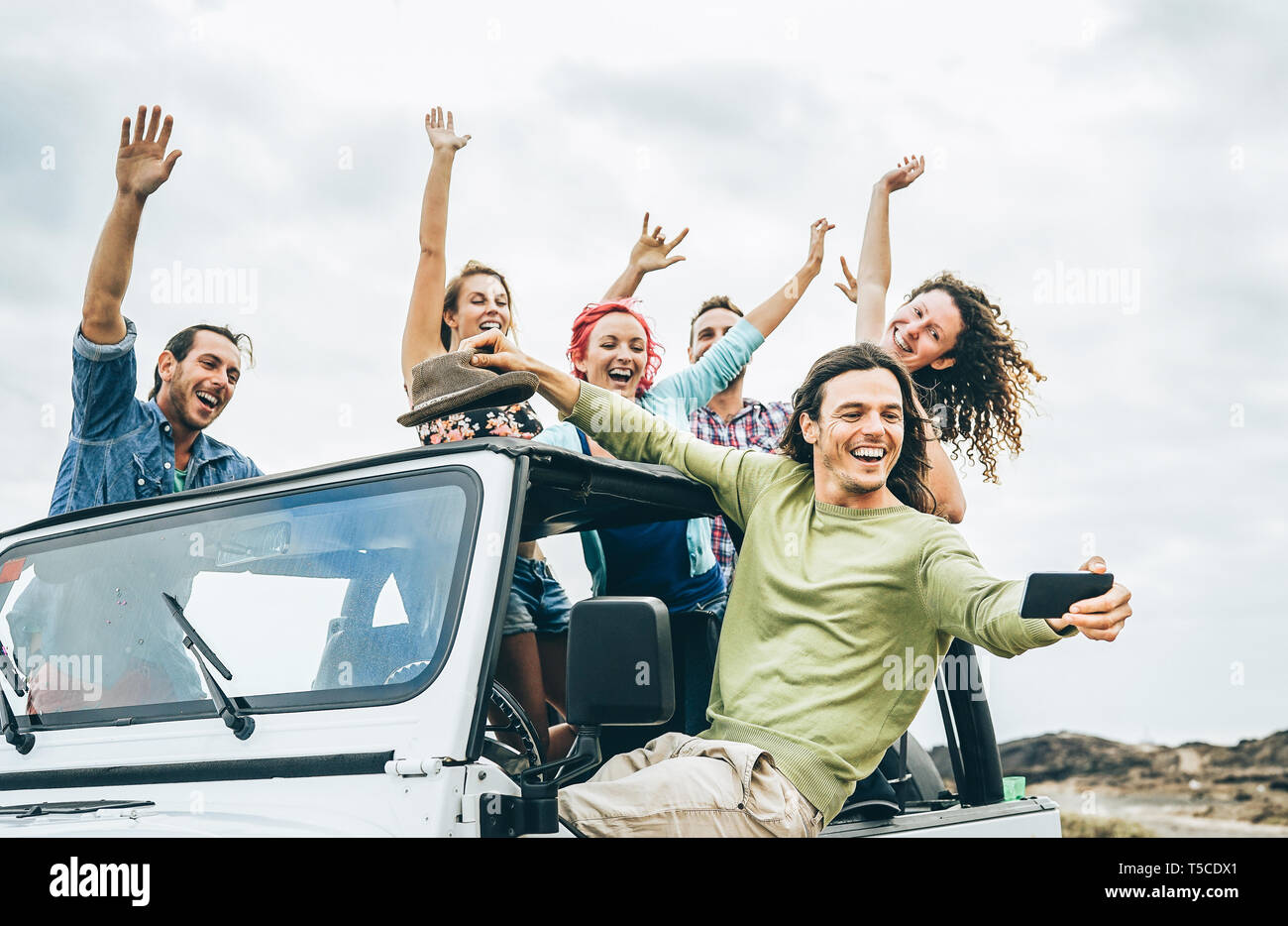 Group of happy friends taking selfie with mobile smart phone on jeep car - Young people having fun making photo during their road trip Stock Photo
