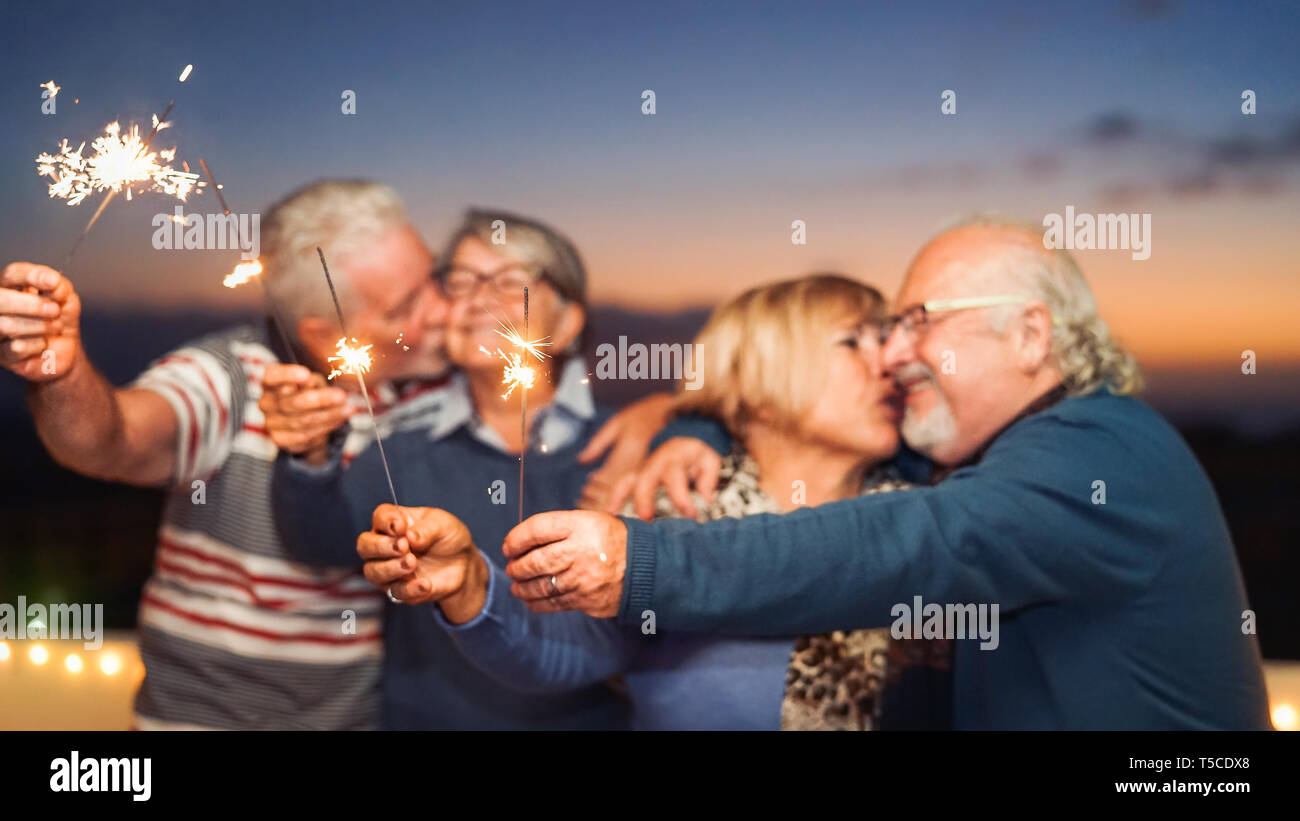 Happy senior friends celebrating with sparklers outdoor - Older people having a fun and tender moment on rooftop Stock Photo