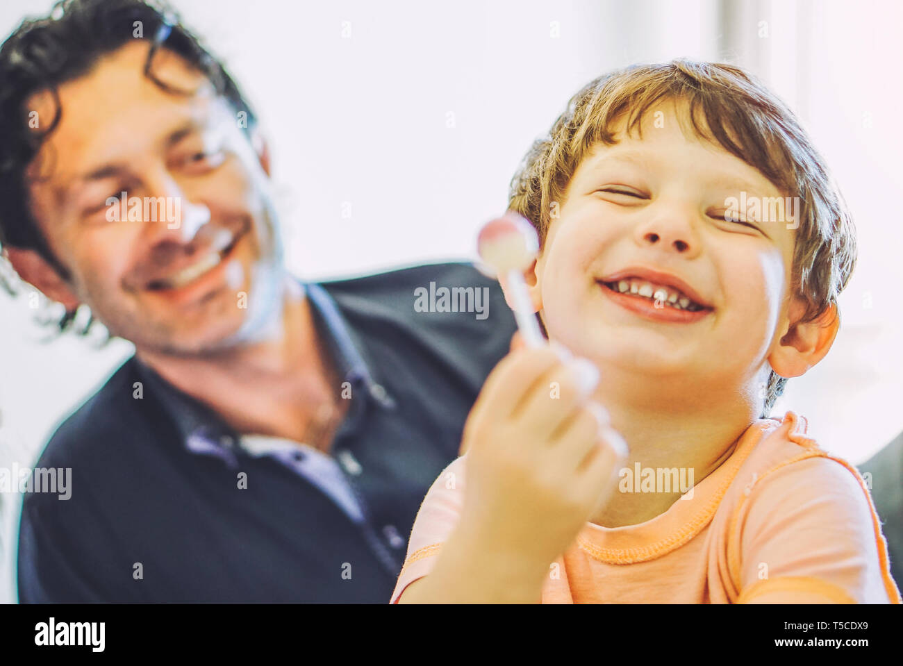 Dad and son having fun together on bed at home - happy family of a child laughing with lollipop in the living room with his father Stock Photo