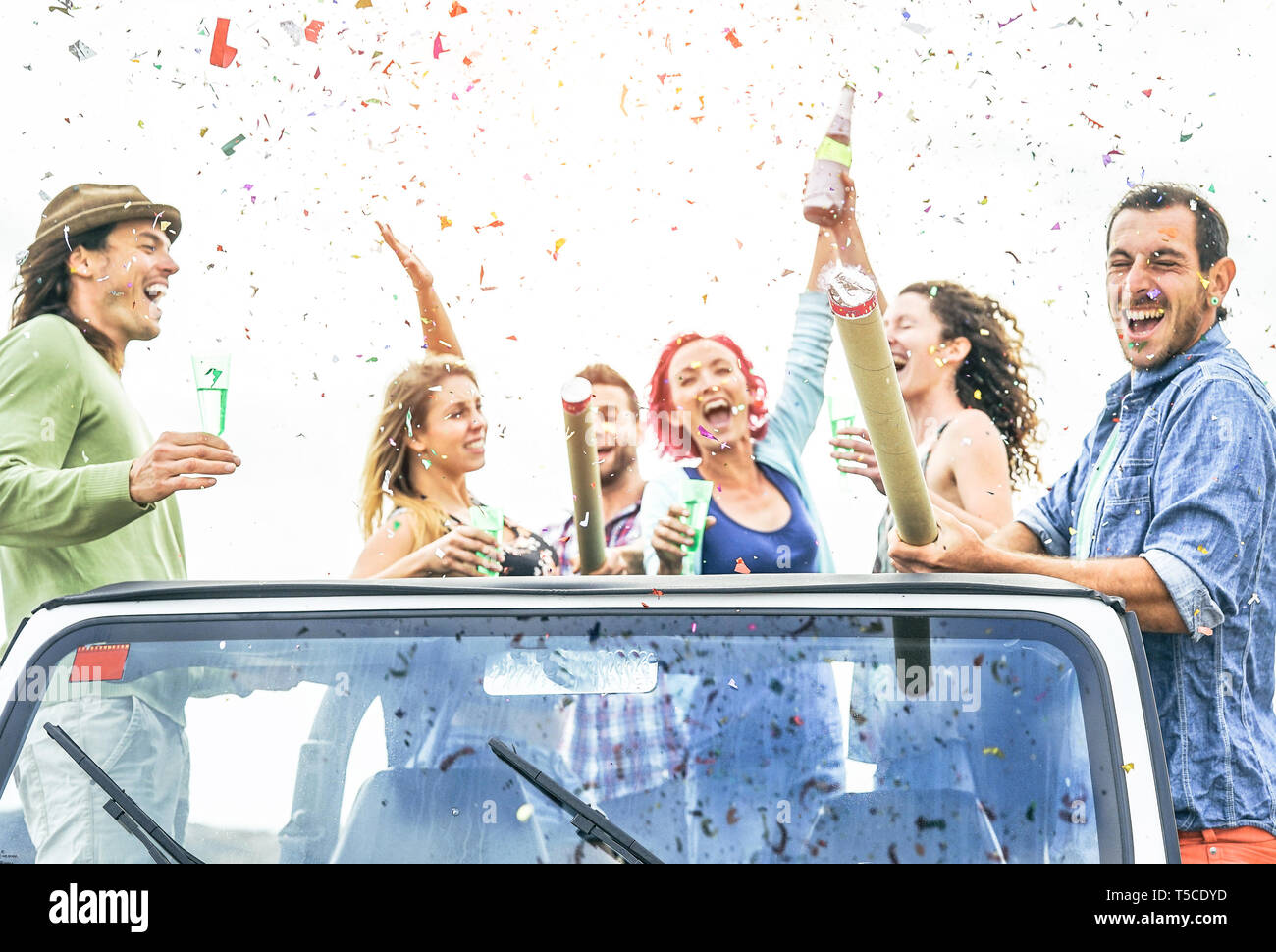 Group of happy friends making party throwing confetti on convertible jeep car - Young people celebrating and having fun drinking champagne Stock Photo