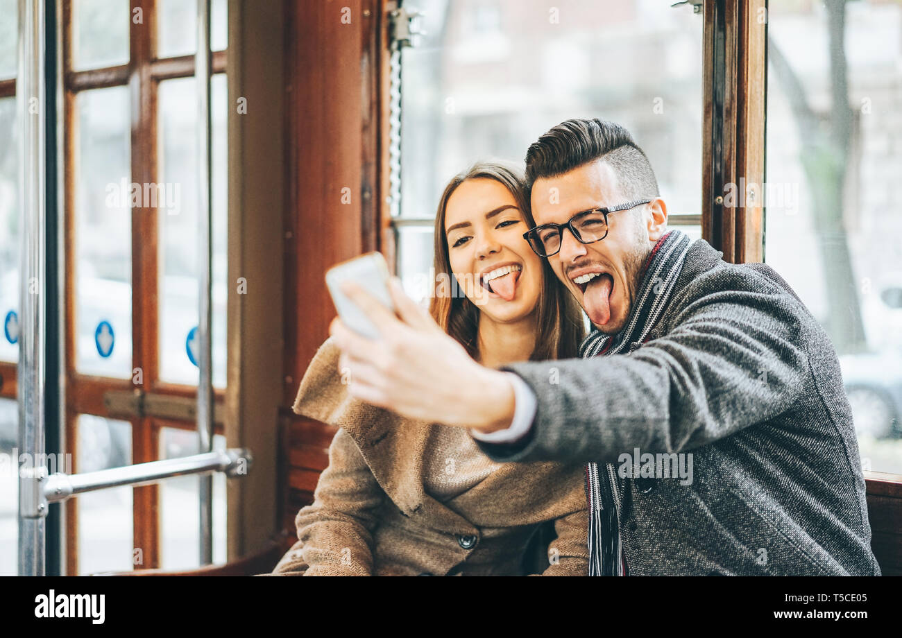 Happy young couple taking photos using mobile smart phone camera inside bus - Travel lovers making a self portrait to post on social media network Stock Photo